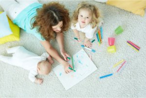 mom with her kids doing art while lying on the floor